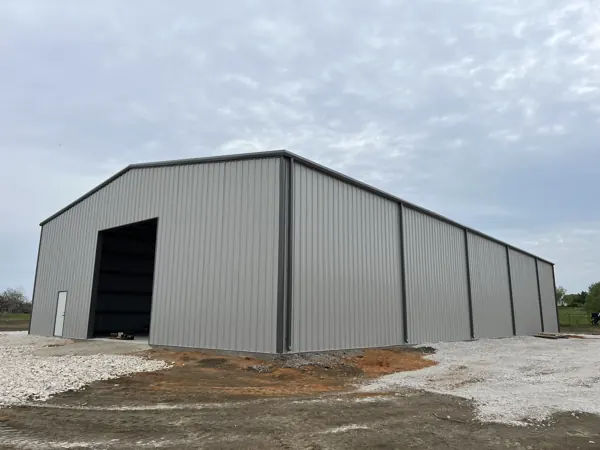 White metal building with a roll-up door on open ground, Howe, TX