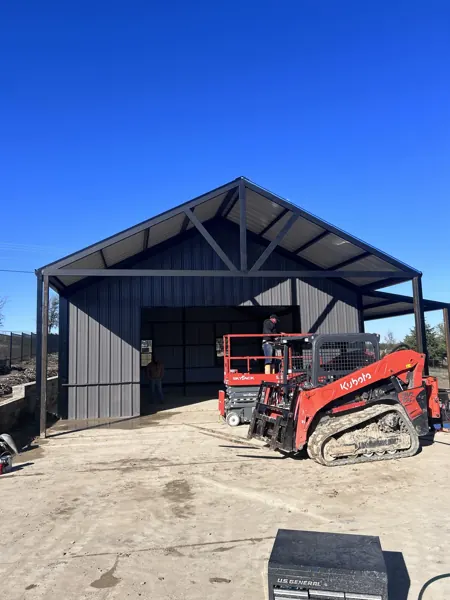 Grey metal shop with a skid steer at the roll-up door, Howe, TX