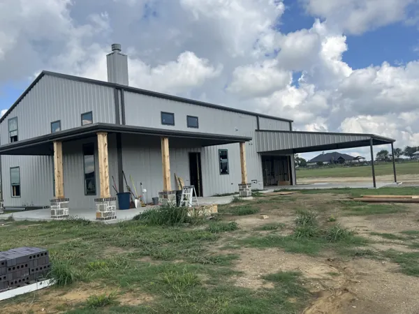 Two-storey grey barndominium with a stone base and covered porch, Sherman, TX