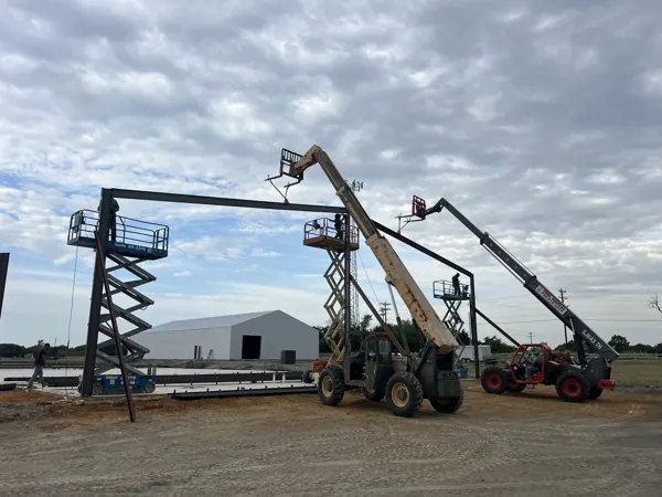 Two boom lifts under a steel frame during erection, Sherman, TX